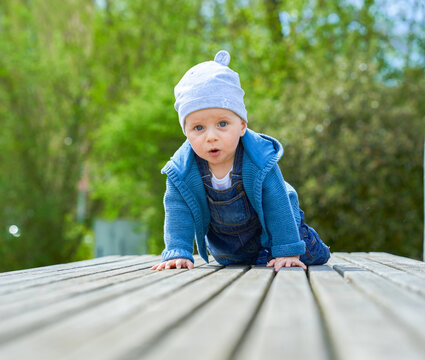 boy up to one year old boy European appearance blue eyes sits in summer on a wooden bench dressed in denim overalls and a light cap