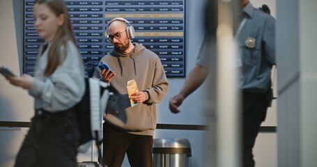 Busy International Airport Terminal: Man in Headphones Using Phone, Taking Selfie, Waiting for...