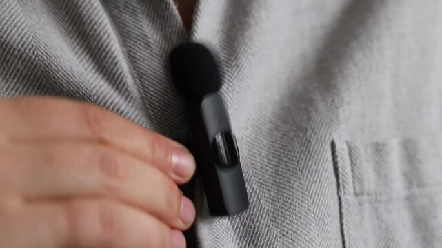 Woman putting lavalier microphone onto her shirt, closeup