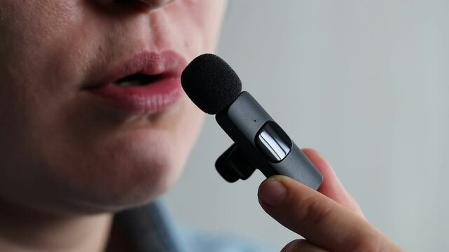 Woman talking into lavalier microphone on light grey background, closeup
