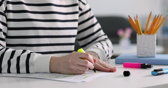Woman highlighting important information at white desk indoors, closeup
