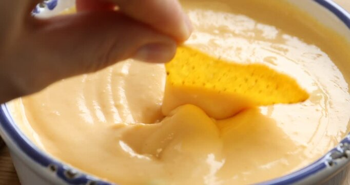 Woman dipping nacho chip into tasty cheese sauce, closeup