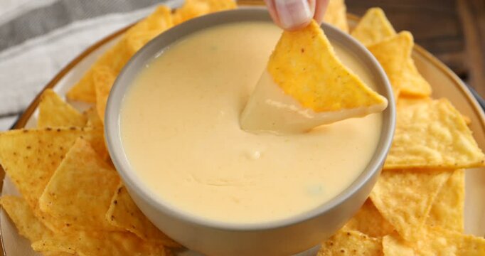 Woman dipping nacho chip into tasty cheese sauce, closeup