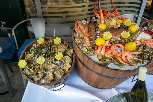Vibrant seafood display featuring oysters, prawns, crab legs, and lemons on ice in wooden barrels at Naschmarkt, Vienna, Austria. Captured at an outdoor market setup showcasing fresh delicacies