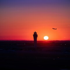 Airplane soaring at sunset near airport control tower with vibrant sky