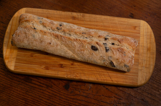 Overhead view of loaf of olive ciabatta bread on wooden cutting board