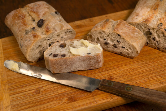 Buttered slice of olive ciabatta bread on wooden cutting board