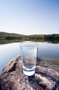 Glass of pure spring water on rock by calm lake