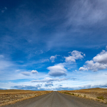 Clouds over empty road in grassy landscape