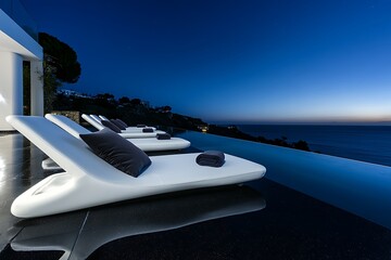 Sophisticated white loungers with charcoal pillows on a glossy black pool deck at night.