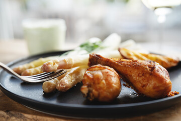 Fresh white asparagus with roasted chicken legs served on black ceramic plate. Horizontal background for delicious, healthy eating. Close-up.