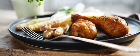 Fresh white asparagus with roasted chicken legs served on black ceramic plate. Horizontal background for delicious, healthy eating. Close-up.