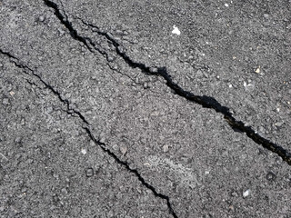 Cracked asphalt road surface background. Surface texture of new asphalt road with cracks. Alligator type cracking in the asphalt pavement. Cracks on asphalt in a afternoon day.