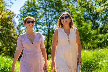 Summer in city. Two beautiful middle aged women enjoying walk in city park on beautiful sunny day....