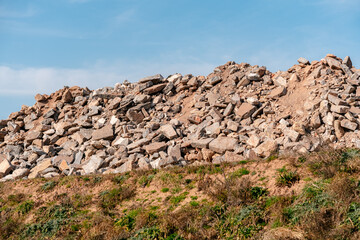 Large pile of rocky debris on a grassy hillside with a clear blue sky. Depicts a landscape of...