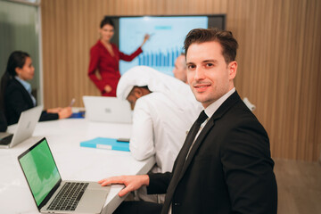 A group of different business people are sitting around a big meeting table in a modern office.
