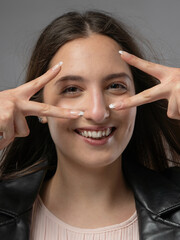 Young woman in a model test, close-up shot. Natural expression, soft smile, and lively emotions. Long hair, leather jacket, neutral background. Visible skin texture, soft studio lighting