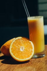 Macro shot of fresh orange cut in half with glass of juice on wooden surface in daylight