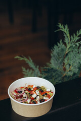 Classic Greek salad with feta cheese, olives and red onion in paper bowl, rustic background with pine