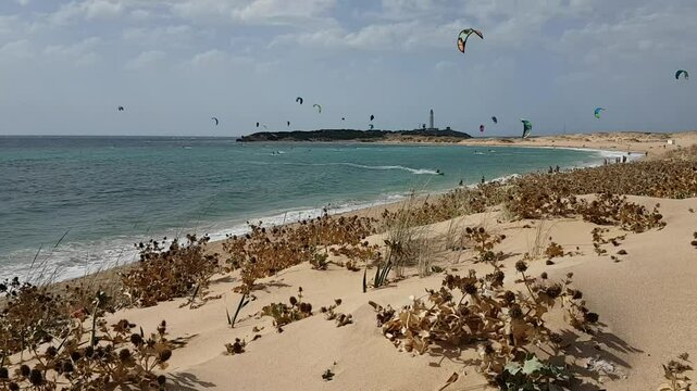 Kitesurfers glide over the waves enjoying on a windy day at the Canos de Meca, a wild, scenic beach along Vejer de la Frontera's coast in Cadiz, Andalusia, Spain.