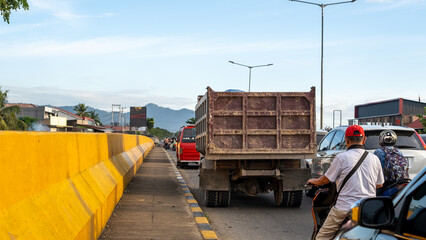 Busy urban street with a truck, motorcyclists, and a vibrant yellow barrier. Vehicles line the...