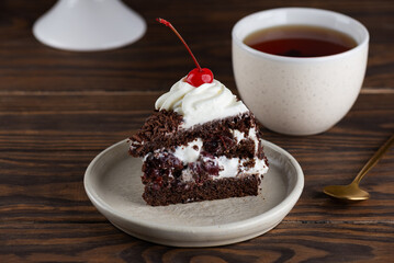 Piece of brownie cake, Black forest or Schwarzwald dessert with chocolate biscuit , whipped cream and cherries in a plate with cup of tea. Vegan dessert.