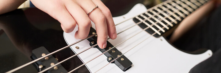 Close-up shot of hand playing electric bass guitar with focus on the strings and frets, highlighting detailed craftsmanship of the instrument in a music setting