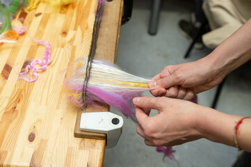 Crafting yarn: female hand combing colorful wool fiber on wooden table