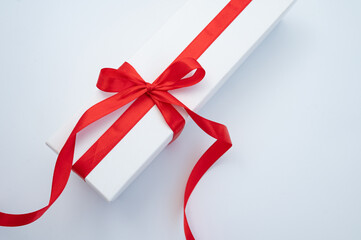 Elegant white gift box with red ribbon on white surface. International Women Week