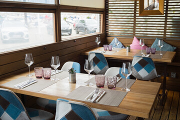 Cozy modern restaurant interior with wooden tables and geometric chairs by large windows