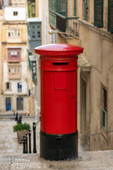 A classic British red post box with "POST OFFICE" inscription, actively used for mail collection on the historic streets of Malta's cities