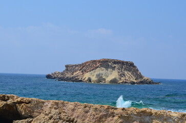 Rocky island amidst turquoise sea with blue sky and waves near coast