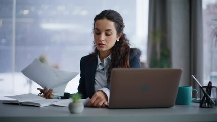 Confident businesswoman managing paperwork reviewing documents at laptop closeup