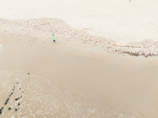 A woman walks along a tranquil beach during winter surrounded by soft sand and gentle ocean waves The scene captures the serene atmosphere of the coastline in cooler weather