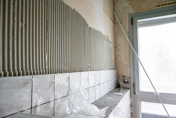 Un gros plan sur le carrelage fraîchement posé dans une salle de bains en rénovation, avec les croisillons insérés entre chaque carreau pour un alignement précis.