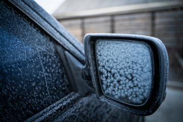 The side rearview mirror of the car is covered with snowflakes from frost. The heating in the car...