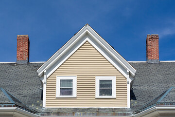 Prominent gable dormer with twin windows and brick chimneys on a historic home in Brighton, Massachusetts, USA
