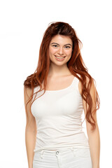 Fototapeta premium Smiling young woman with long red hair, wearing white tank top. Isolated on white background
