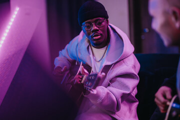 A group of multiracial musicians engage in a collaborative session, playing guitars in a cozy studio with ambient lighting, fostering creativity and expression.