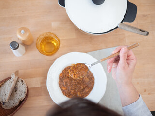 Woman eating lentil soup at wooden table with bread and drink