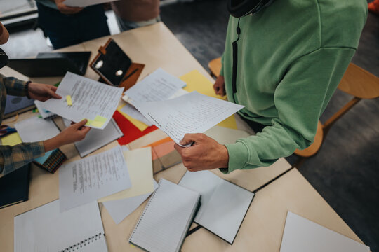 A group of students working together on school assignments in a classroom. Papers and notebooks are spread on the table as they collaborate.