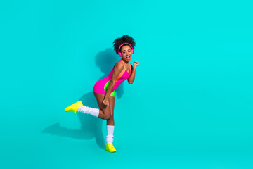 Fototapeta premium Cheerful young woman in vibrant sportswear posing confidently against teal backdrop, showcasing active lifestyle