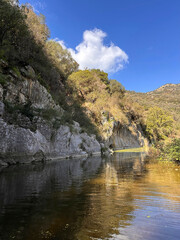 Obraz premium Sicily Gole di Tiberio Serene river flowing between rocky cliffs under a clear blue sky with lush greenery reflecting on water healthy nature concept