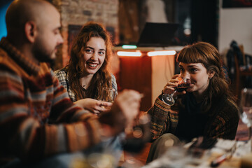 A group of three friends is seen socializing and enjoying wine in a warm interior ambiance, showcasing happiness, friendship, and relaxation in a casual domestic setting.