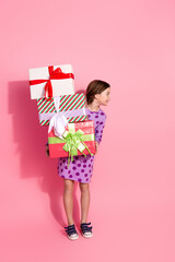 Cheerful young girl in stylish attire holding festive presents against a bright pink background,...