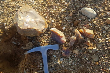 Fragments of colored chalcedony split by a geological hammer, search for rocks and minerals in a quarry, field photo