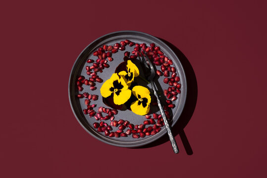 Edible Pansy Flowers with Pomegranate Seeds on Maroon Plate