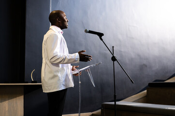 Man giving presentation at podium, engaging audience with gestures, at conference hall, copy space