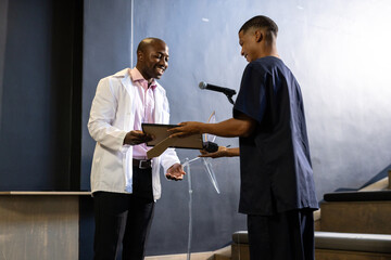 man receiving award from colleague at podium during ceremony, at office, at conference hall