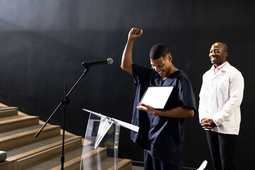 Celebrating achievement on stage, man with certificate, at conference hall, copy space
